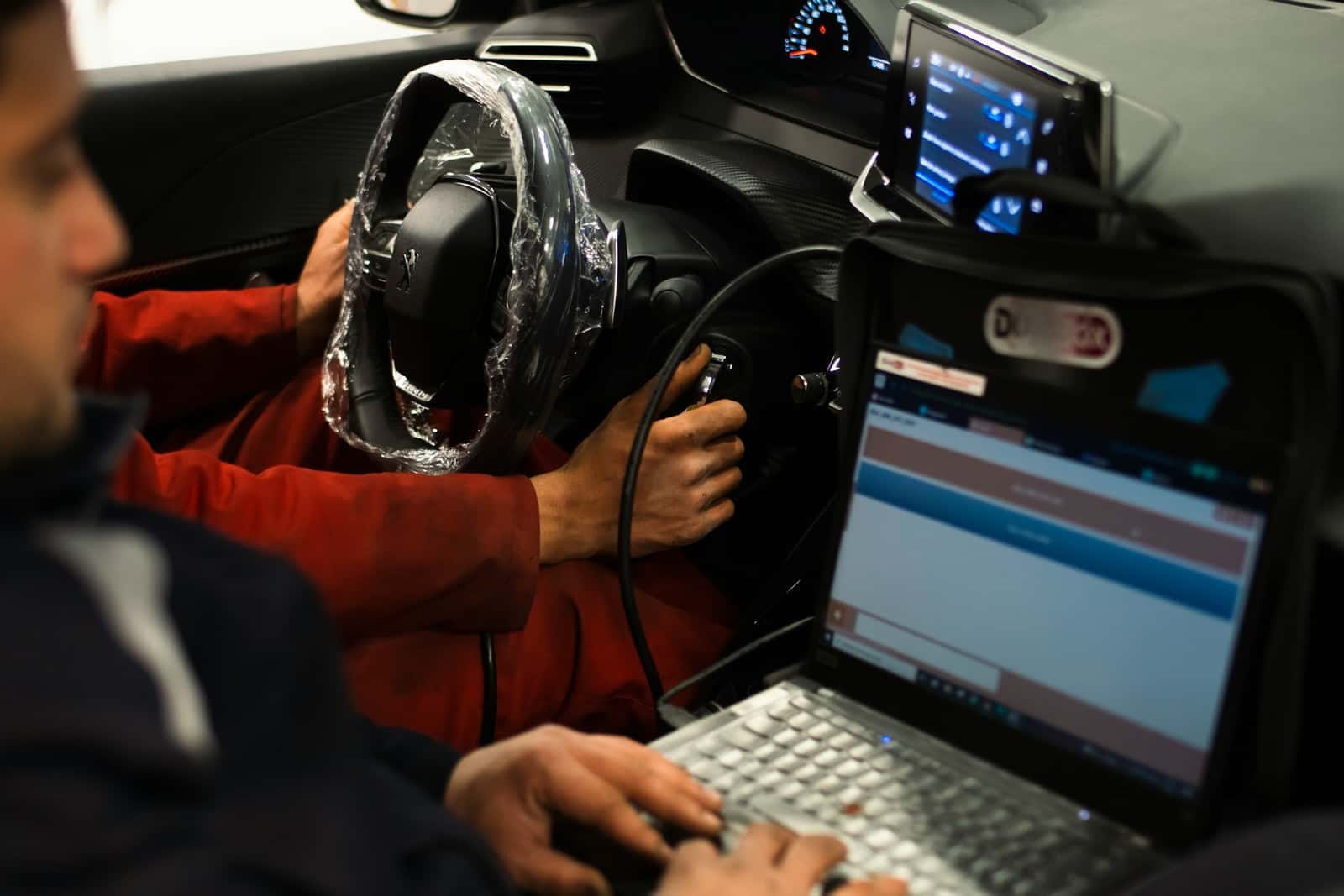 Mechaniker im Auto, ein Laptop ist per Kabel an die Diagnosebuchse angeschlossen